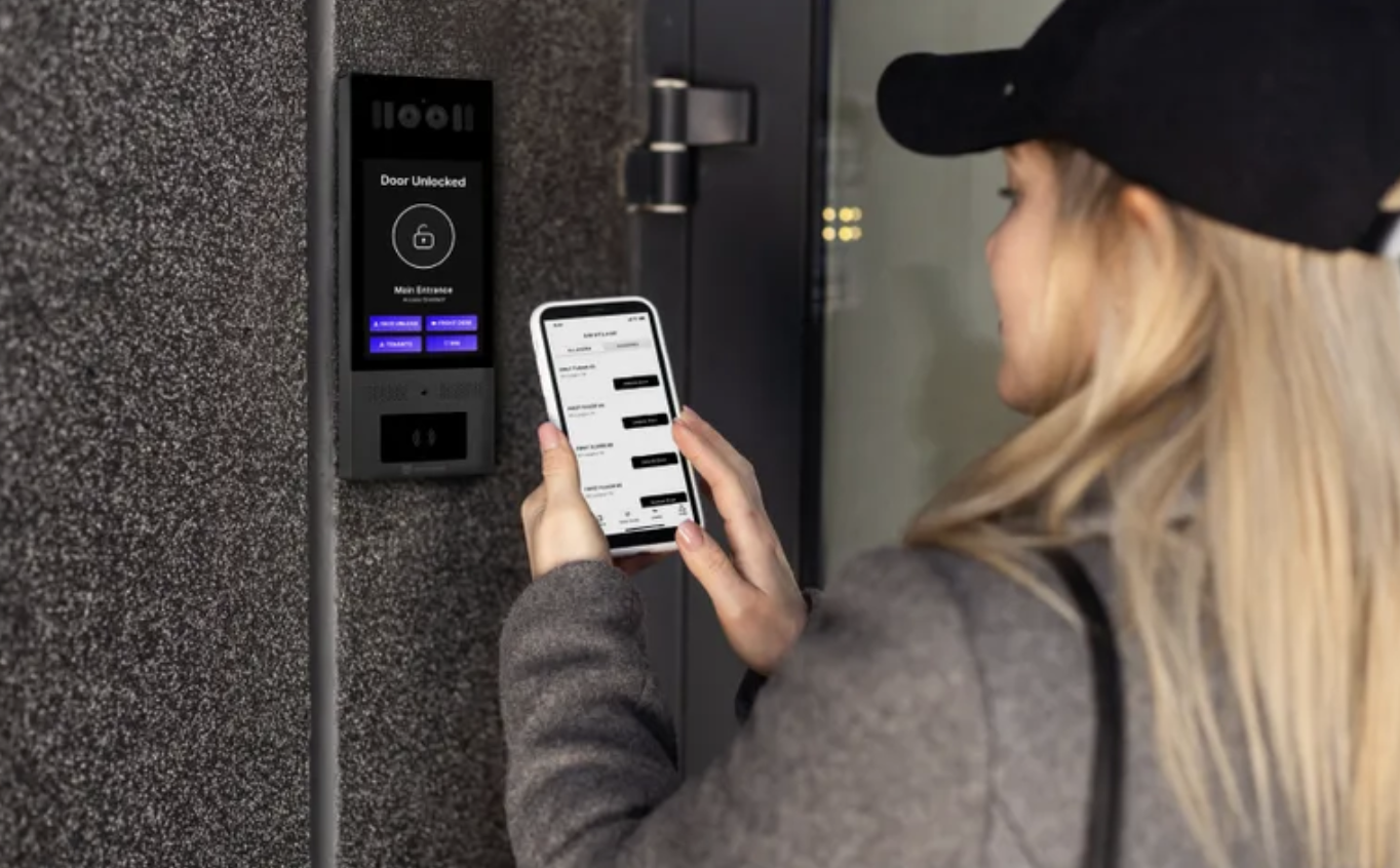 Resident using smartphone app to unlock apartment door via video intercom panel showing door unlocked status