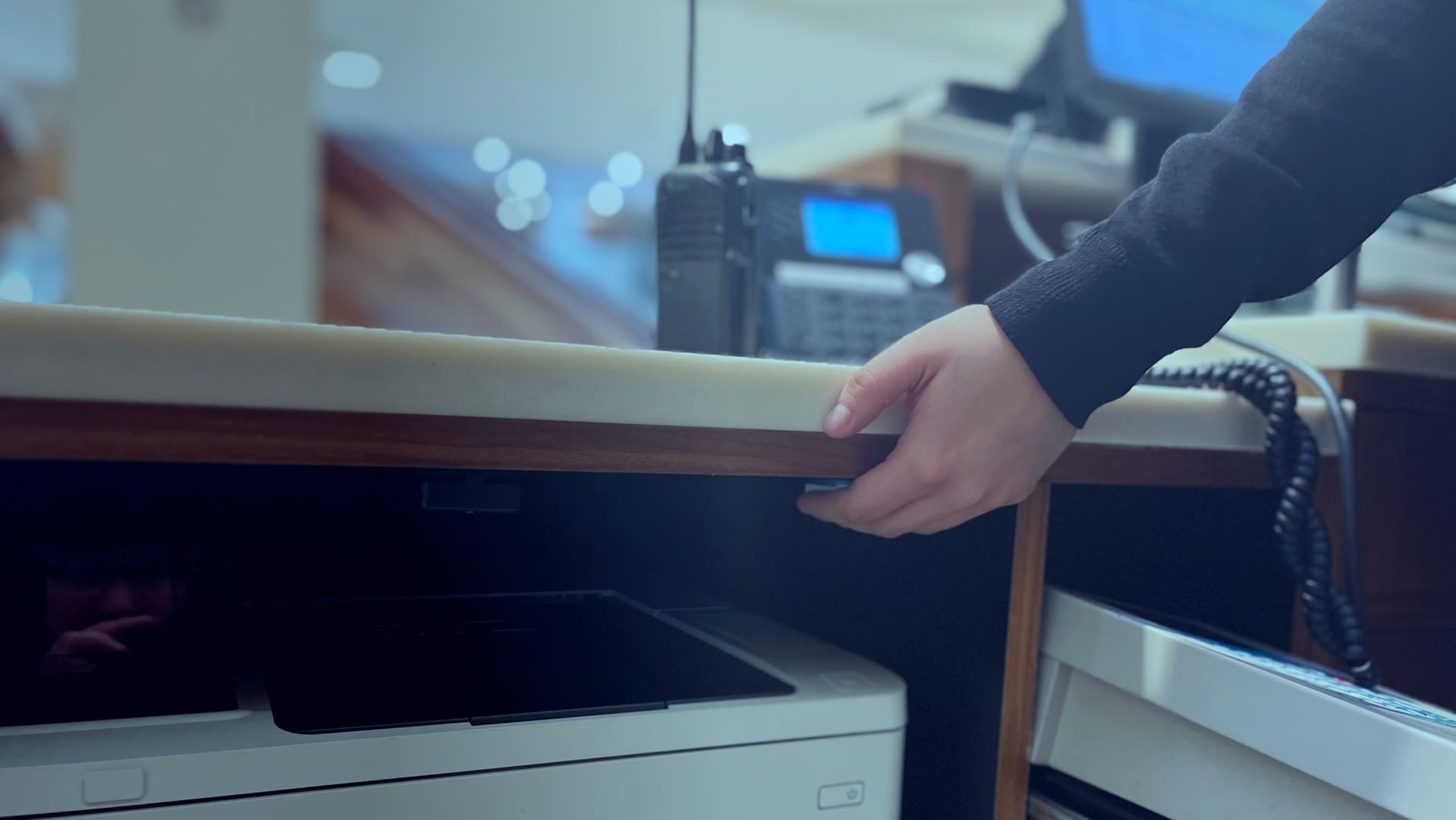 Employee hand reaching under desk to press discreet panic button for emergency alert